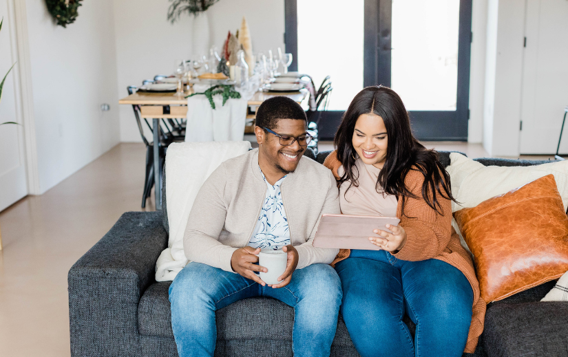 Happy couple sitting on a couch, browsing a tablet together, representing online store traffic and digital shopping trends.